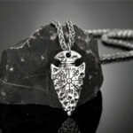 Collier Vegvisir ointe de lance de couleur argenté composé d'une chaine et son pendentif mit en valeur en étant posé sur un morceau de roche noir.